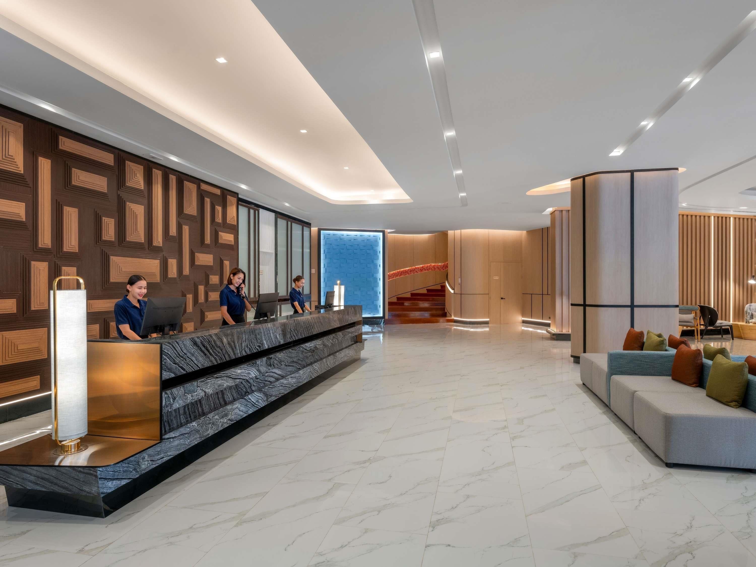 Un moderno vestíbulo de hotel con mostrador de recepción, escalera y zona de estar.