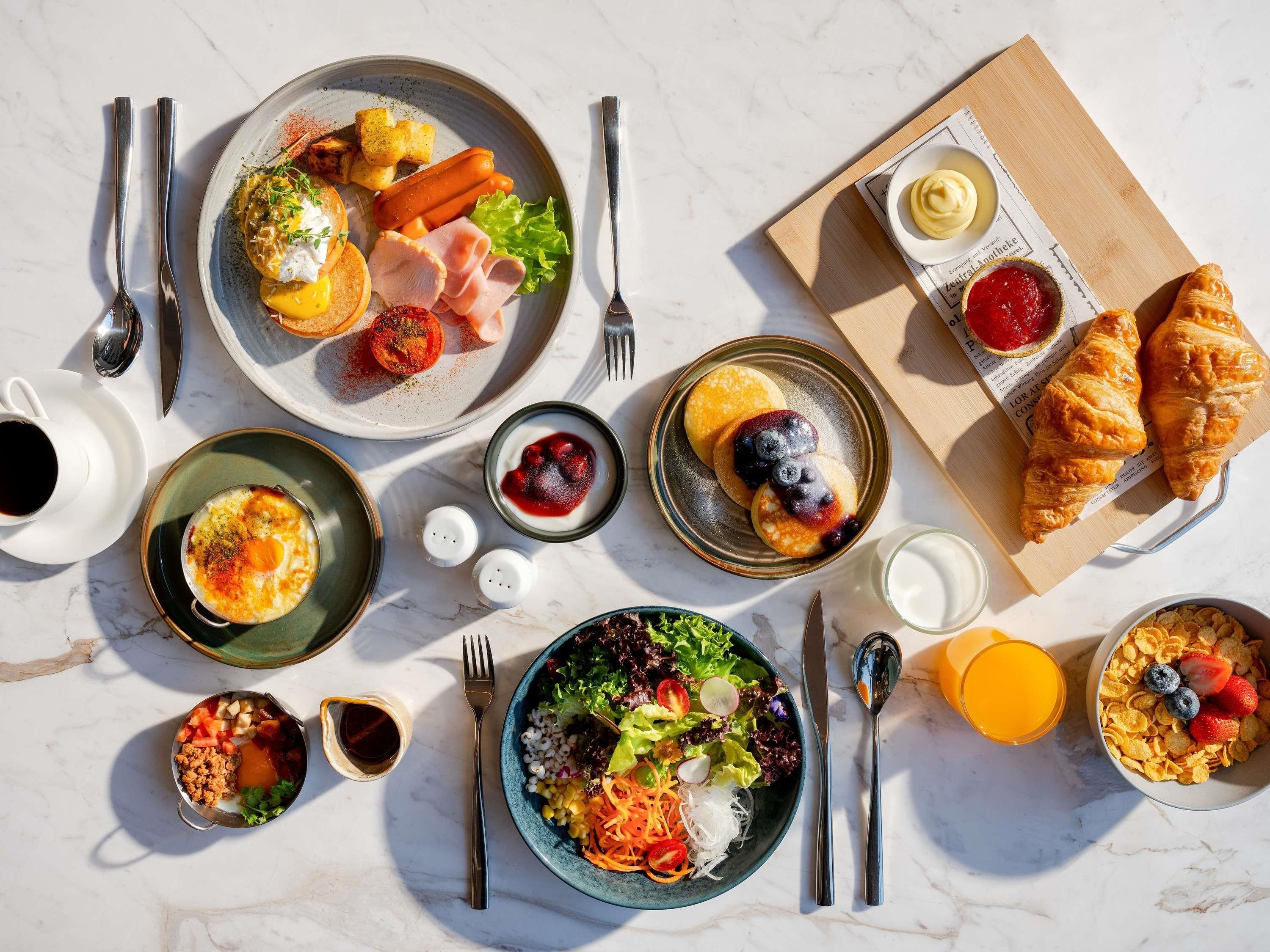 A breakfast setting with various dishes including eggs, pancakes, croissants, and a bowl of cereal.