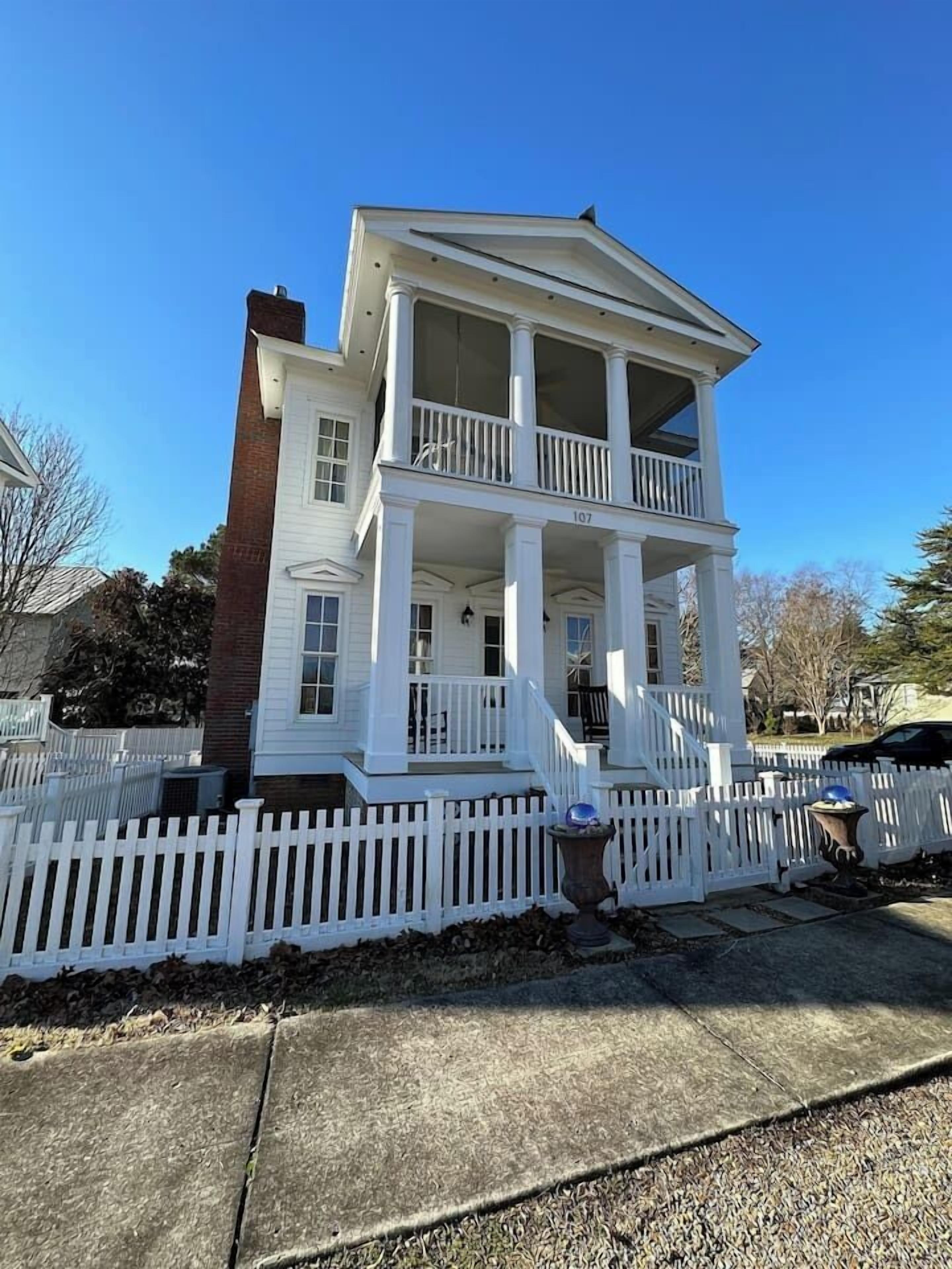 A two-story house with a balcony, a white picket fence, and a brick chimney.