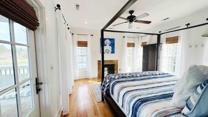 A bedroom with a large bed, a ceiling fan, a fireplace, and a view of the outdoors. - Scenic Cottage w/ Trails, Pond & Valley Views (Pisgah)