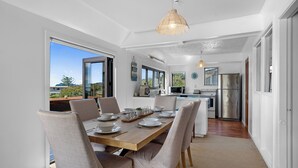 A modern kitchen with stainless steel appliances, a dining area with a wooden table and chairs, and a view of the outdoors. - Pohara Beach Escape - Pohara Beach Holiday Home (Pohara Beach)