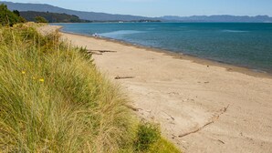 A beach with clear blue water, sandy shore, and distant mountains. - Pohara Beach Escape - Pohara Beach Holiday Home (Pohara Beach)