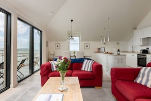 A modern apartment with a red sofa set, a wooden coffee table, a vase with flowers, and a view of the sea through large windows.