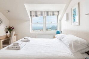 A bedroom with a bed, a desk, a chair, a window with a view, and a radiator.