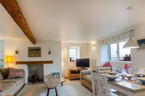 A cozy living room with a sofa, a coffee table, a TV, and a dining area with chairs and a table set for a meal.