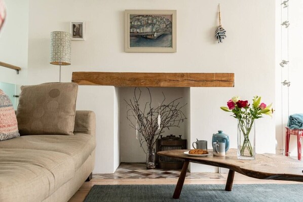 A living room with a sofa, a fireplace, a table with a vase of flowers, and a painting on the wall.