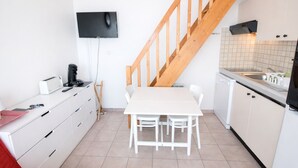 Kompakti keittiö, jossa on ruokapöytä, valkoiset kaapit, puinen portaikko ja seinälle asennettu taulutelevisio.