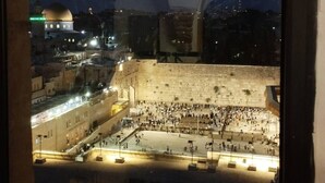 Une vue à travers une fenêtre en arc d’un site historique, avec une vaste place ouverte, un bâtiment imposant surmonté d’un dôme et une foule de personnes.