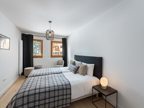 A modern bedroom with two beds, a small table, and a hanging light fixture.
