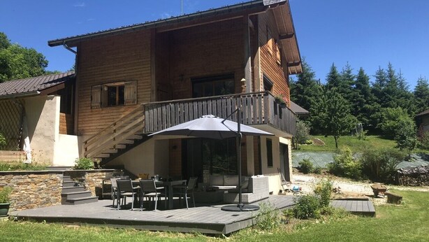 Et toetagers træhus med balkon, terrasse med udendørs møbler og en velplejet have.