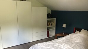 Et soveværelse med en seng, et hvidt klædeskab, en reol og et natbord.