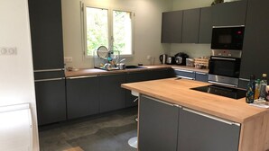 Et moderne køkken med mørke skabe, en træbordplade og stålemmer, herunder en mikroovn, ovn og kaffemaskine.
