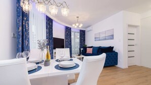 Un'elegante zona pranzo moderna con un tavolo bianco apparecchiato per due, un lampadario e un divano blu sullo sfondo.