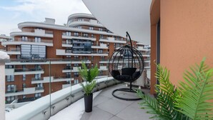 Un balcone con una sedia a dondolo, piante in vaso e vista sugli edifici vicini.