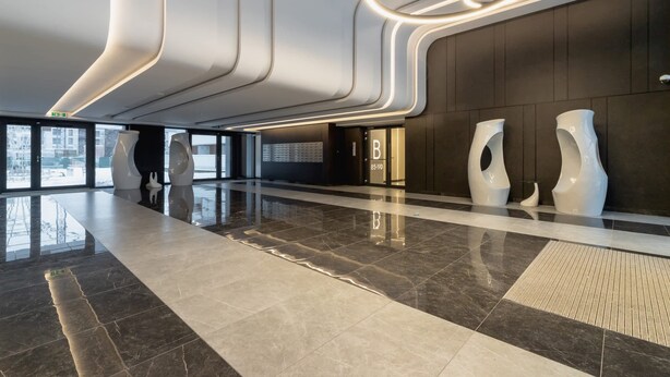 Una hall moderna dal design elegante, con pavimento lucido, opere d'arte contemporanee e un soffitto ben illuminato con plafoniere circolari.