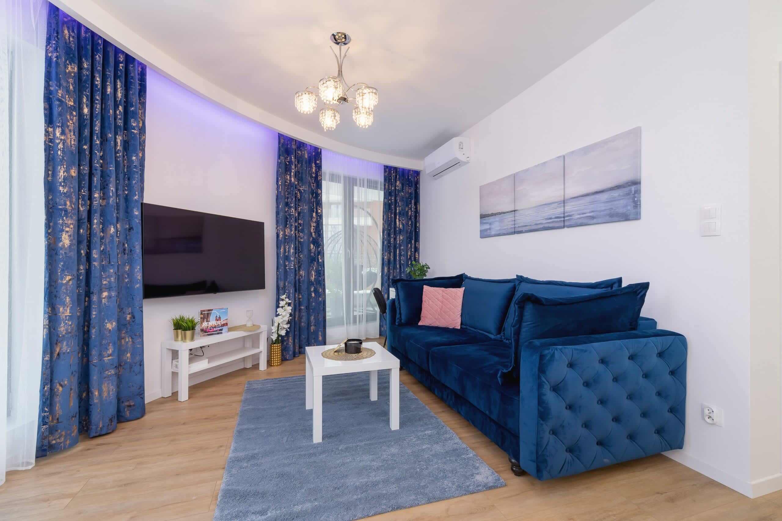 Un salon moderne avec un canapé bleu, une table basse blanche et un téléviseur posé sur un meuble.