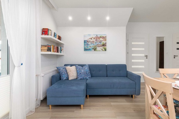 A bright living room featuring a blue sofa, a wooden dining table, and a large window.