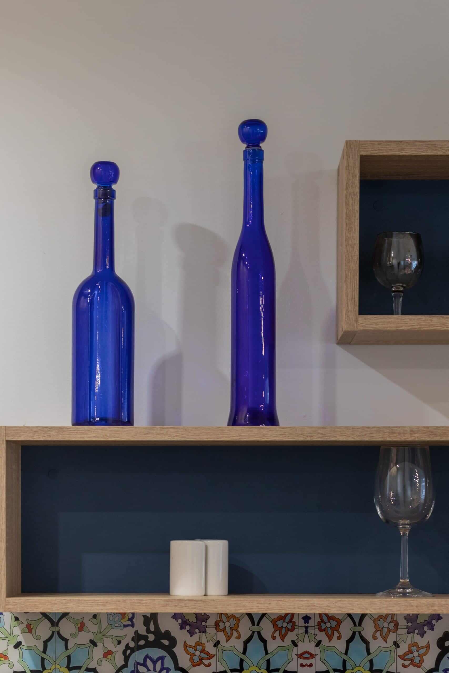 A shelf with two blue bottles and a framed picture of a wine glass.