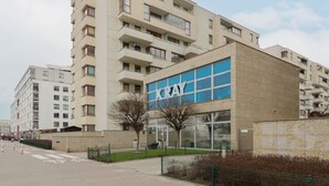 Un edificio moderno con un llamativo letrero 'Kray', que presenta una fachada combinada de vidrio y ladrillo, y un sendero peatonal en la parte delantera.