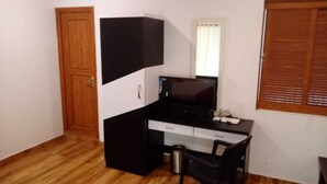 A small room with a wooden door, a black desk with a computer, a chair, and a window with blinds. - Oxygen Rainforest Resort (Thodupuzha)