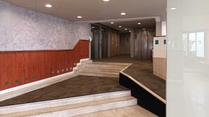 Eine moderne Hotelhalle mit einer Marmortreppe, einer Rezeption und einem Aufzug.