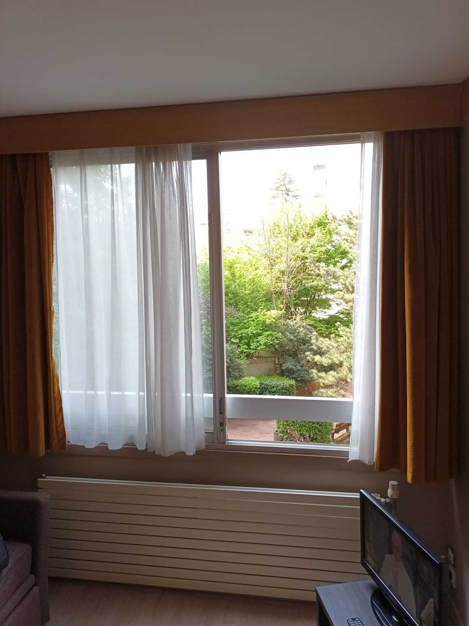Habitació amb una finestra gran, un radiador a sota i un televisor sobre un suport.
