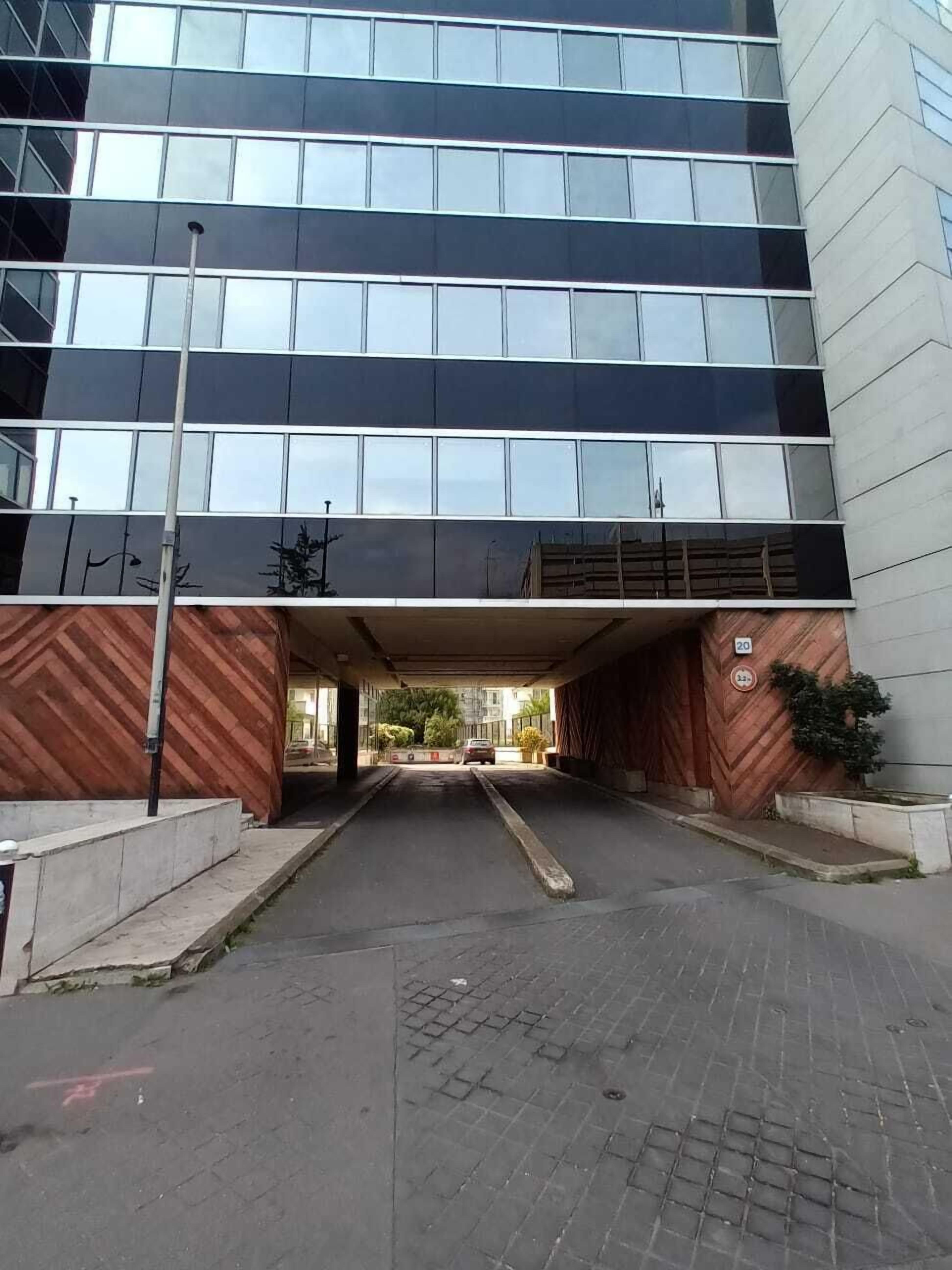 Ein modernes Gebäude mit großem Eingangsbereich, überdachtem Parkplatz und einem Ziegelweg, der zum Eingang führt.