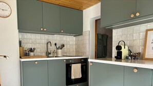 Une cuisine avec des armoires de couleur turquoise, un dosseret de carreaux blancs, un four noir et un plafond en bois.