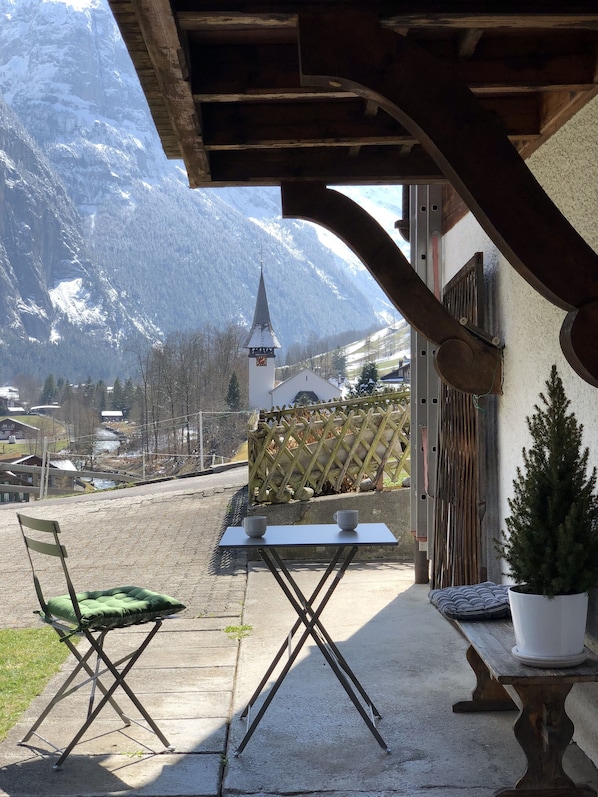 A patio with a table and chairs, a potted plant, and a view of a mountain and church.