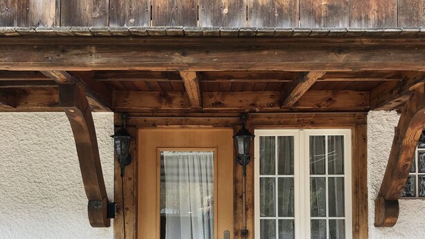 Un bâtiment rustique en bois, doté d’une porte en bois, d’une fenêtre avec des rideaux, d’une petite plante en pot et d’un banc à l’extérieur.