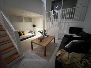 A modern living room with a staircase, a sofa, a coffee table, and a TV. - Barbican Pad by condokeeper (London)