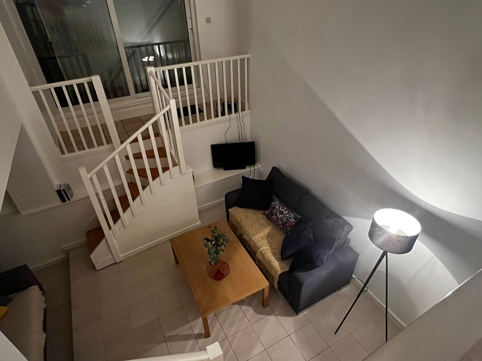 A living room with a staircase, a sofa, a coffee table, and a floor lamp.