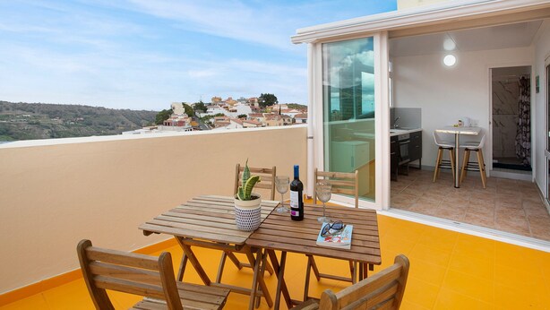 A balcony with a wooden table, chairs, a potted plant, a bottle, and glasses. - Holiday Apartment "Carmelo Y Carmela 6" with Mountain View, Private Terrace & Wi-Fi (Teror)