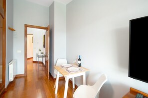Un coin repas avec une table dressée pour deux personnes, une bouteille de vin et un téléviseur fixé au mur.