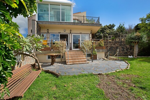 Une maison à deux étages avec une terrasse en pierre, un banc en bois et un escalier menant à un balcon.