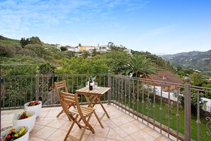 Un balcon avec une table et des chaises, des plantes en pot et une vue panoramique sur une colline.