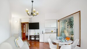 A modern living room with a sofa, a dining table with chairs, a TV, a kitchen area, and a large window with a view. - Holiday Apartment "Carmelo Y Carmela 2" with Mountain View, Private Terrace & Wi-Fi (Teror)