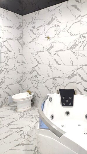 A bathroom with marble-patterned walls, a white pedestal sink, and a modern bathtub with control panels.