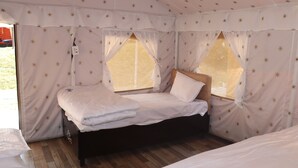 Um quarto tipo tenda com uma cama, uma mesinha e uma janela.