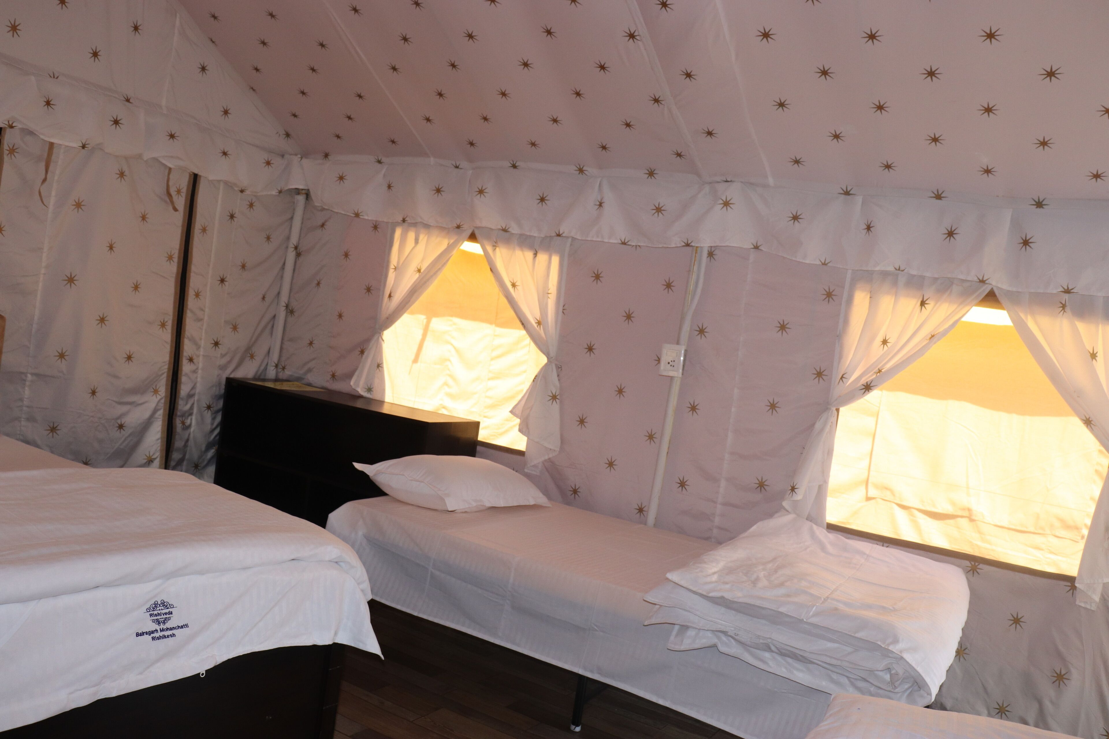 A tent with two beds, each with white bedding and star-patterned curtains.