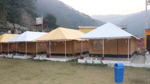 Fileira de tendas com área gramada na frente, uma lixeira azul e montanhas ao fundo.