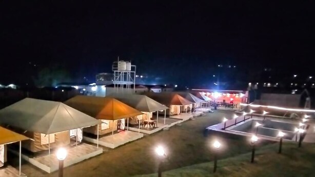 Fileira de tendas iluminadas, um reservatório de água e um edifício com luzes ao fundo.