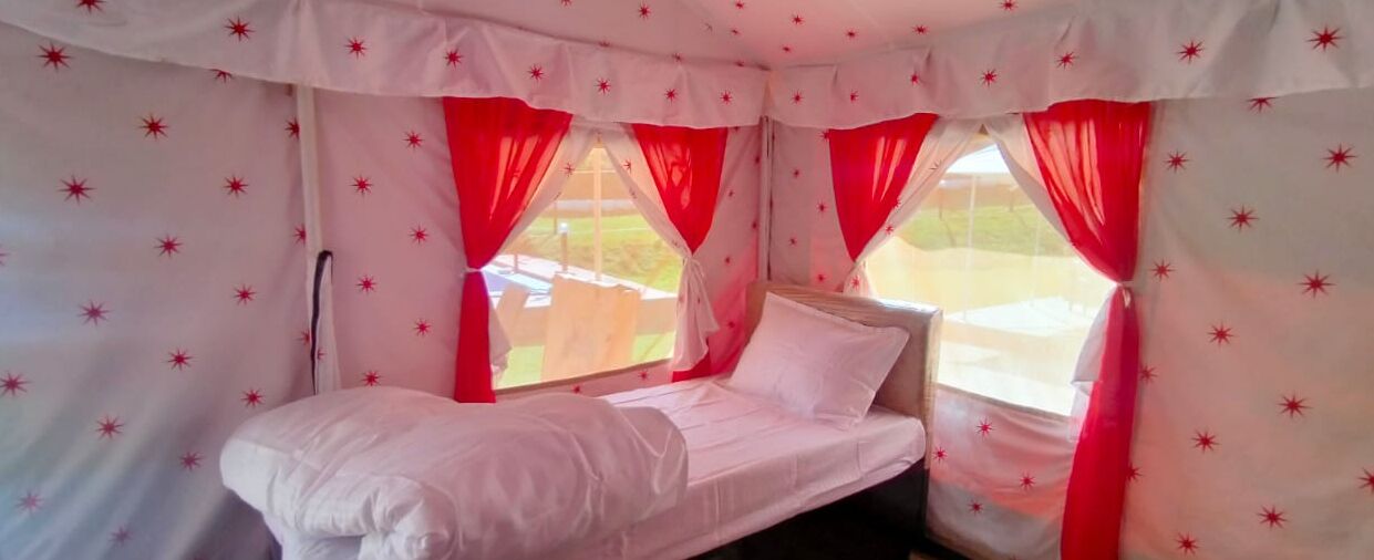 A single bed with white bedding in a room with red curtains and star-patterned wallpaper.