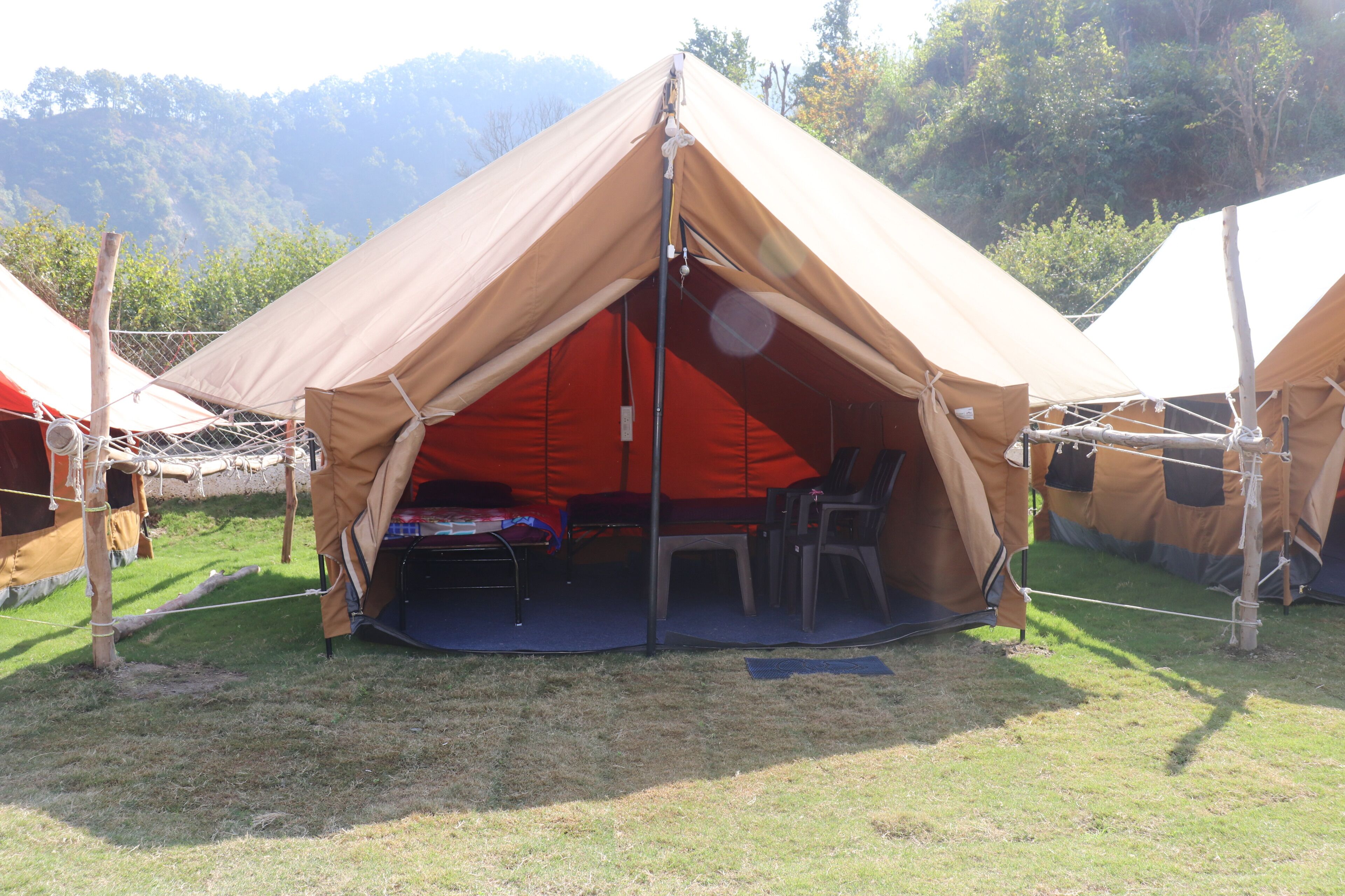 A large, beige tent with a red interior, set up on a grassy field with mountains in the background.