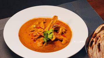 A plate of curry with chicken and a side of flatbread, accompanied by a small bowl of sauce and sliced onions.