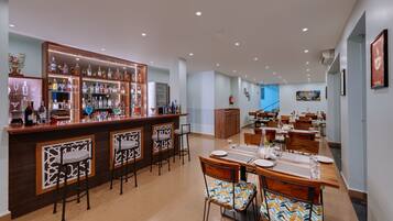 A spacious dining area with a long wooden table set for a meal, a bar with a variety of bottles, and a modern kitchen in the background.