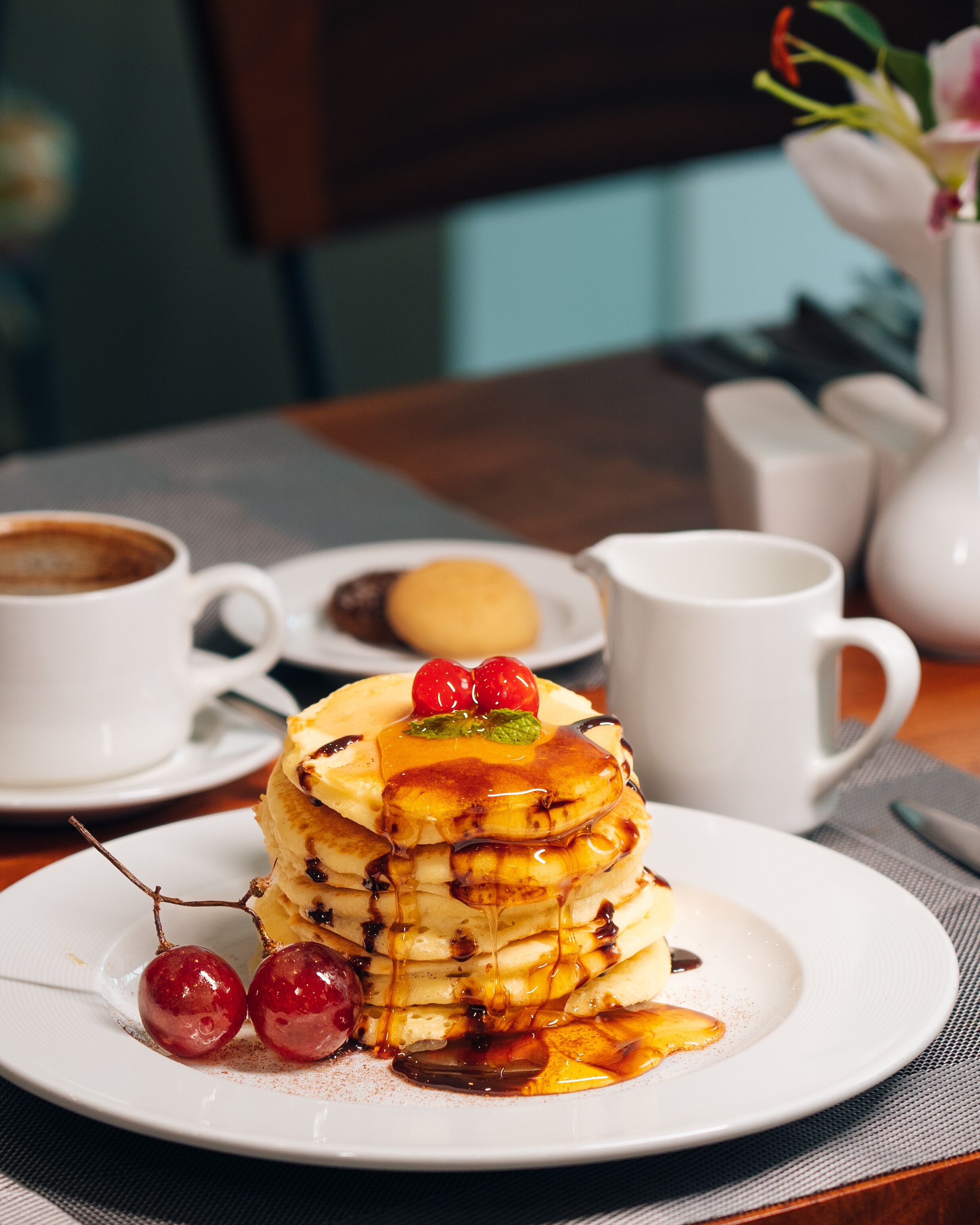 Ein Frühstücksteller mit Pfannkuchen, Kirschen und Sirup, dazu eine Tasse Kaffee und ein Muffin.