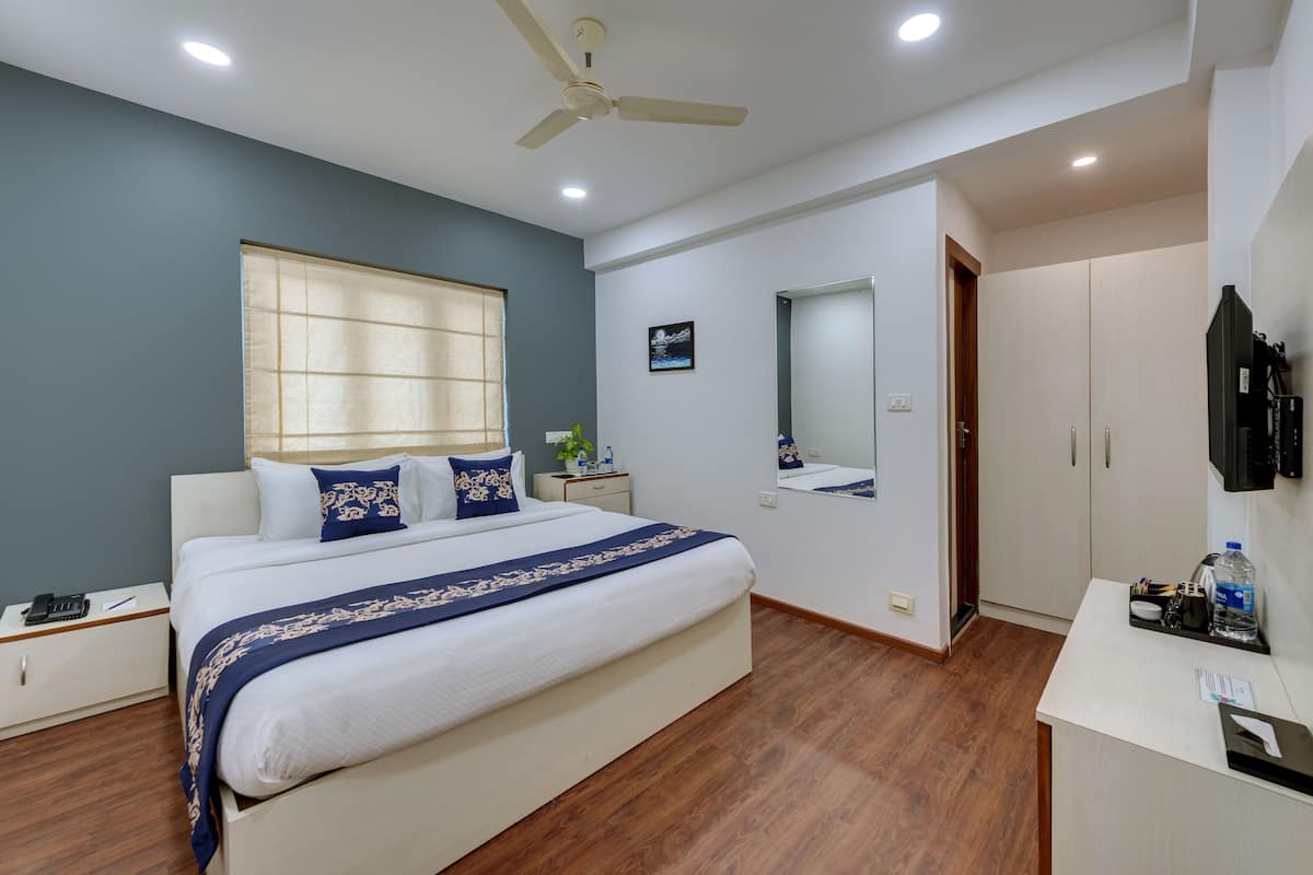 Une chambre à coucher comprenant un lit, des tables de chevet, un ventilateur de plafond, une fenêtre avec des stores, un miroir et une armoire.