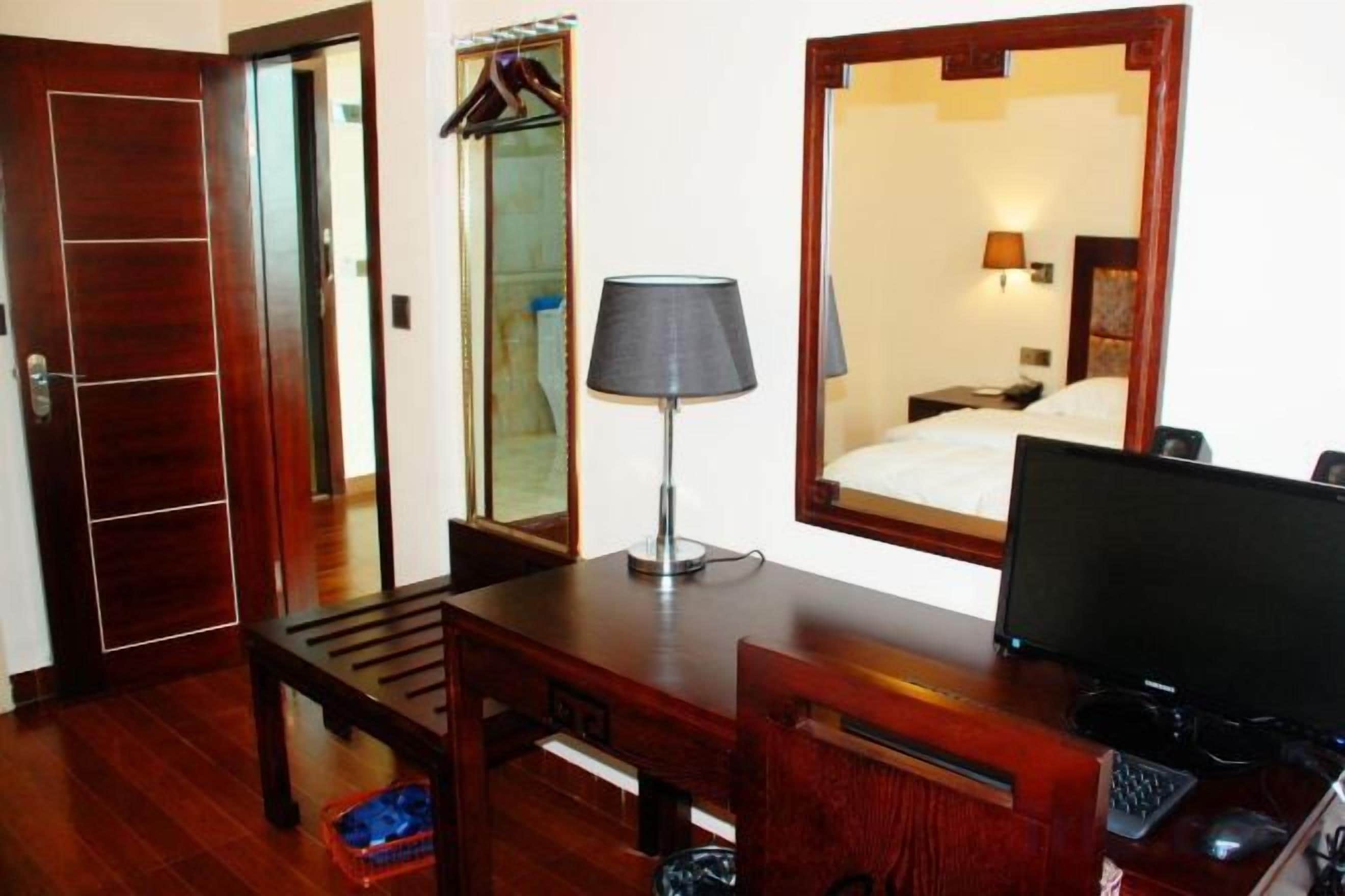 Una habitación de hotel con un escritorio de madera, una lámpara, un espejo y una cama.