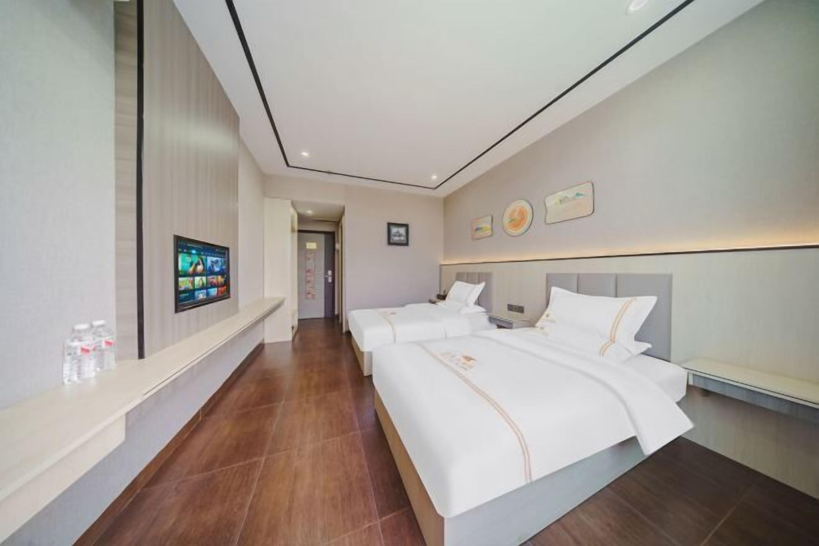 Una habitación de hotel con dos camas, un televisor en la pared y un baño visible a través de una puerta abierta.